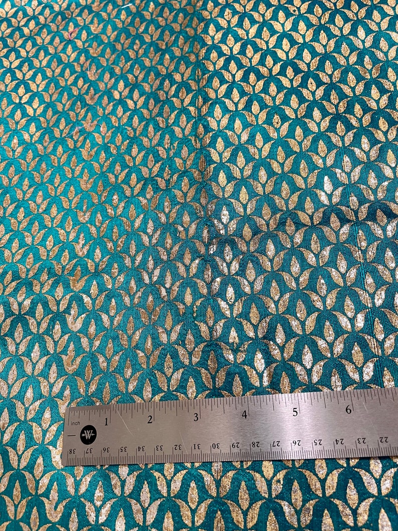 May include: Teal fabric with a gold leaf pattern. The fabric is measured with a ruler showing 6 inches.