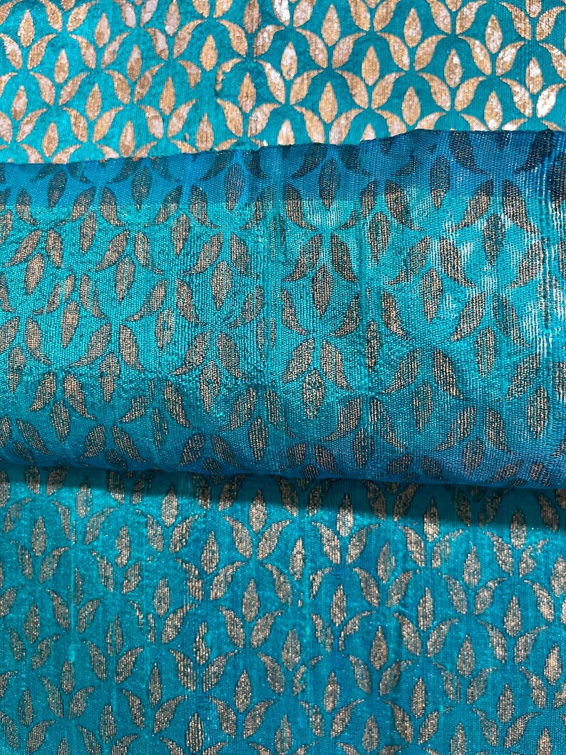 May include: Teal fabric with a silver leaf pattern. The fabric is folded in half, showing the pattern on both sides.
