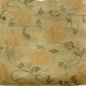Könnte beinhalten: Ein durchsichtiger Stoff mit einem floralen Muster in Grün- und Goldtönen. Die Blumen sind mit kleinen, glänzenden Perlen verziert.