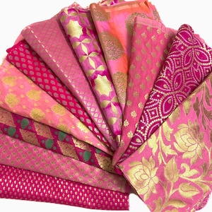 May include: A collection of pink and gold fabric scraps with various patterns, including floral, geometric, and paisley designs.