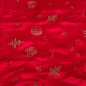 May include: Red fabric with a repeating pattern of gold embroidered flowers and leaves.