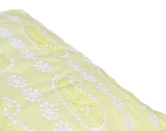 Può includere: Un cuscino giallo con motivi paisley e floreali ricamati in bianco.