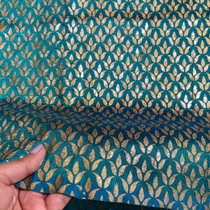 May include: Teal fabric with a gold leaf pattern. The fabric has a subtle sheen and is perfect for upholstery or crafting projects.