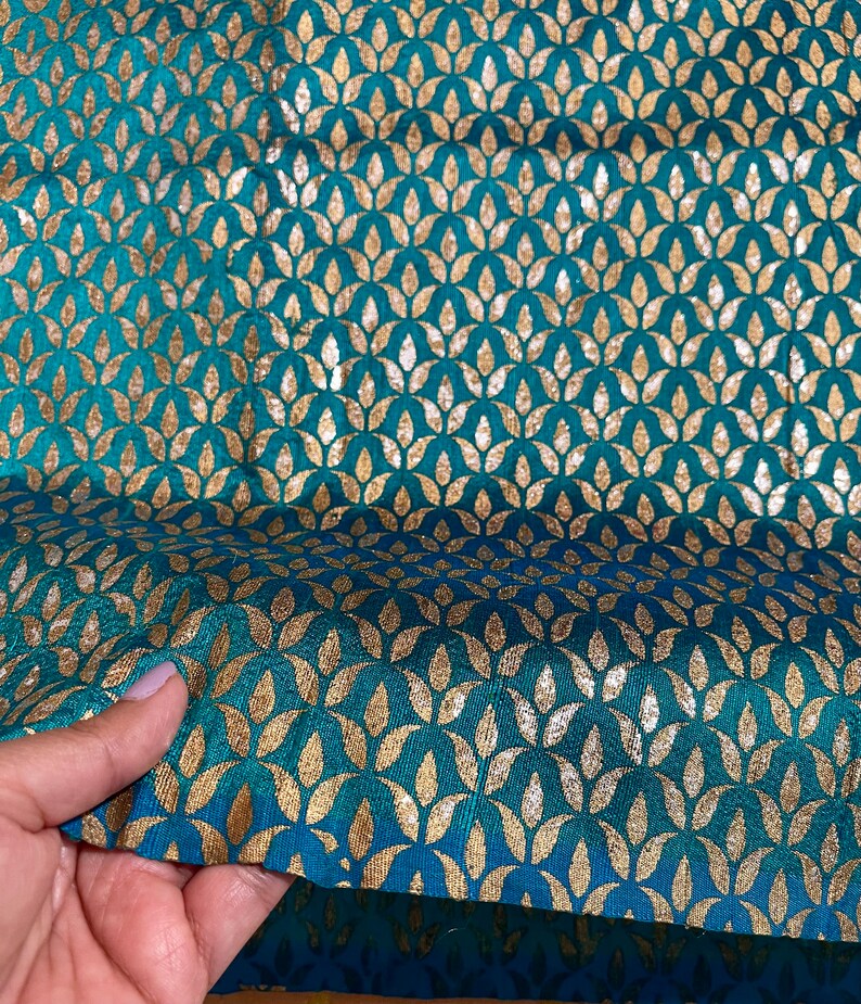 May include: Teal fabric with a gold leaf pattern. The fabric has a subtle sheen and is perfect for upholstery or crafting projects.