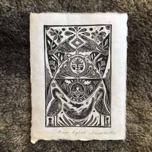 May include: Black and white woodcut print of a stylised design featuring birds, flowers, and geometric shapes. The print is titled "River Reflect" by "Scarred Brittles".