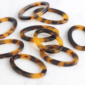 Op de afbeelding: Ovale schildpad kralen. Deze harskralen hebben een mix van bruine en amberkleurige tinten. De kralen hebben een gladde, glanzende afwerking en zijn ideaal voor het maken van sieraden. De ovale vorm is ongeveer 3,8 cm lang.