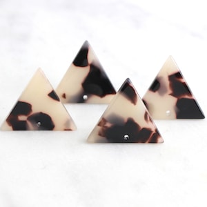 May include: Four white and brown triangle-shaped resin embellishments with a hole in the center.