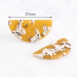 Puede incluir: Dos componentes de pendientes de acrílico en forma de semicírculo. Los componentes son de color amarillo mostaza con vetas blancas y negras. El componente superior mide 37 mm de ancho. Cada componente tiene un pequeño agujero.