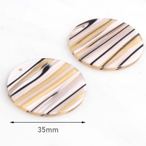 May include: Two round, 35mm, white, black, and gold striped resin embellishments with a hole in the top.