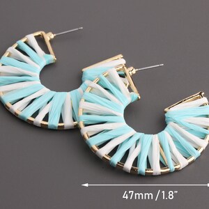 May include: A pair of hoop earrings made of woven white and light blue fabric with a gold metal frame. The earrings are 47 mm in diameter.