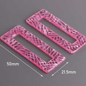 Peut inclure: Deux boucles d'oreilles rectangulaires en acrylique rose avec un motif marbré. Les boucles d'oreilles mesurent 50 mm sur 21,5 mm.