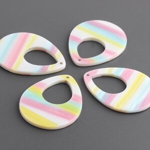 May include: Four colorful teardrop-shaped resin earrings with a hole at the top. The earrings are white with pink, blue, and yellow stripes.