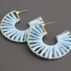 May include: A pair of hoop earrings with a woven design in shades of blue and white. The hoops are made of gold metal.