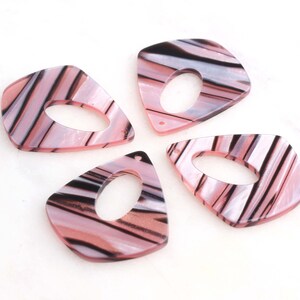 May include: Four pink and black striped acrylic pendant charms with a hole in the center. The charms are shaped like a teardrop with rounded edges.
