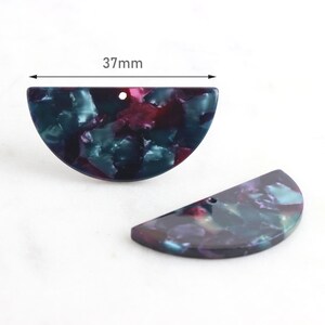 Pode incluir: Duas peças de resina em forma de semicírculo com um padrão de mármore em tons de azul-esverdeado, roxo e preto. As peças têm um furo perfurado na parte superior e medem 37 mm de diâmetro.