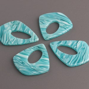 Op de afbeelding: Vier teal en witte marmerachtige plastic hangers met een gat in het midden. De hangers zijn traanvormig met een afgeronde bovenkant en een puntige onderkant.