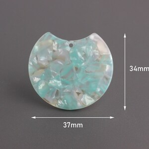 May include: A turquoise and white marbled plastic pendant with a hole at the top. The pendant is 37 mm wide and 34 mm tall.