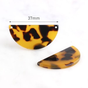 May include: Two half-circle shaped tortoise shell patterned resin pieces with a hole at the top. The larger piece measures 37 mm across.