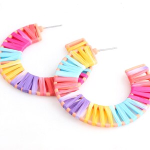 May include: A pair of rainbow coloured hoop earrings. The hoops are made of a woven material and are a bright and cheerful colour.