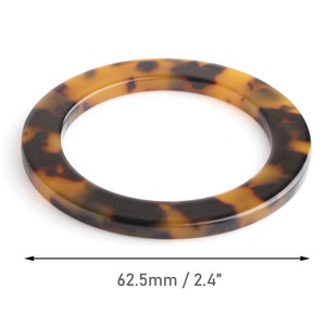 May include: A round, tortoiseshell-patterned ring with a diameter of 2.4 inches. The ring is made of a glossy material, featuring a mix of brown and amber tones. The object is isolated on a white background.