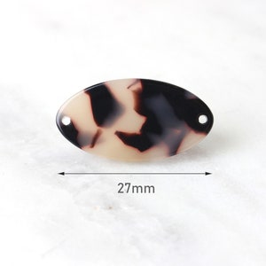 Könnte beinhalten: Ovale Schildpatt-Acrylperle mit zwei Löchern. Die Perle ist 27 mm lang und hat ein Muster aus schwarzen und beigen Wirbeln. Ideal für die Schmuckherstellung und Bastelarbeiten.