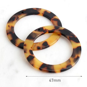Op de afbeelding: Twee bruine en zwarte kunststof ringen met een schildpadpatroon en een gat in elk. De ringen hebben een diameter van 47 mm.