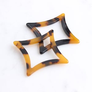 May include: Two tortoiseshell hair clips in the shape of a star. The clips are made of a brown and black plastic material.