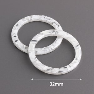 May include: Two white resin rings with a marbled pattern. The rings are 32 mm in diameter.