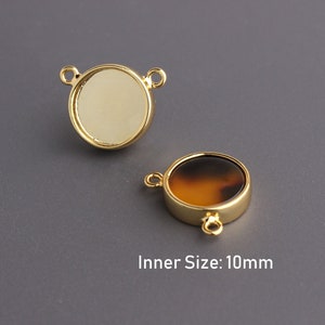 May include: Two gold-toned metal round pendant settings with a 10mm inner size. One setting is empty and the other has a brown and orange tortoiseshell-like cabochon.