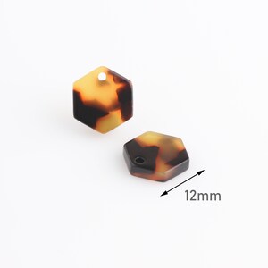 Pode incluir: Dois pingentes hexagonais de resina na cor marrom, amarelo e preto com um furo na parte superior. Cada pingente mede 12 mm de largura.