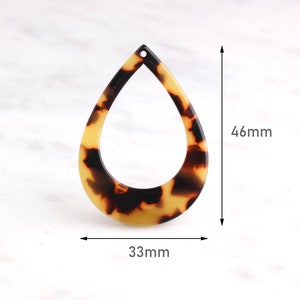 May include: A brown and yellow teardrop-shaped pendant with a hole at the top. The pendant is 46 mm tall and 33 mm wide.