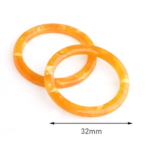 May include: Two orange resin bangles with a marbled effect, interlocked on a white background. The diameter of the bangles is 32mm. These accessories are suitable for everyday wear.