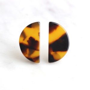 May include: A pair of half-circle earrings with a tortoiseshell pattern in shades of brown, yellow, and black.