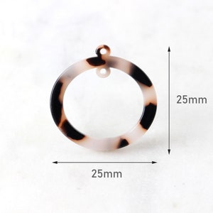 May include: A white and brown tortoiseshell plastic circle with a hole in the center. The circle is 2.5 inches in diameter.