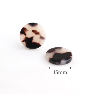 Könnte beinhalten: Zwei runde Knöpfe mit Schildpattmuster, einer aufrecht und einer flach liegend. Die Knöpfe sind cremefarben, braun und schwarz. Der Durchmesser der Knöpfe beträgt 1,5 cm.