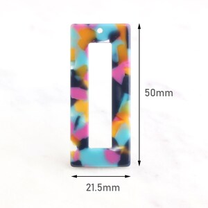Puede incluir: Un componente rectangular para pendientes con un colorido patrón de terrazo en tonos azules, rosas, amarillos y negros. El pendiente mide 2,15 cm de ancho y 5 cm de largo. Tiene un pequeño agujero en la parte superior para la fijación.