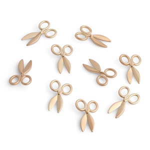 May include: Ten gold-colored miniature scissors scattered on a white background.