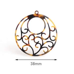 May include: A round, openwork pendant with a tortoiseshell pattern. The pendant features a central circle and intricate, swirling cutouts. The diameter is 38mm, or approximately 1.5 inches. It has a small loop at the top for hanging.