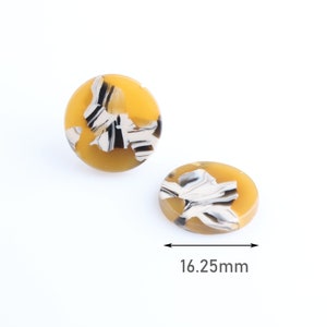 May include: Two yellow and white marbled resin cabochons. One is round, the other is oval. The cabochons have a black, white, and tan pattern. The oval cabochon measures 16.25mm in length.