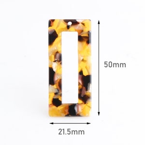 Peut inclure: Un cadre rectangulaire en plastique de couleur jaune, marron et blanc à motifs avec un trou en haut. Le cadre mesure 21,5 mm de large et 50 mm de haut.
