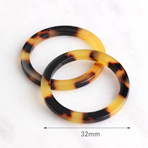 May include: Two brown and yellow tortoiseshell plastic rings, each with a diameter of 32 mm.