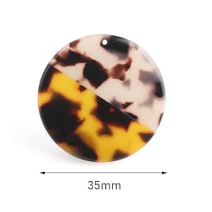 May include: A round, 35mm, tortoiseshell-patterned resin pendant with a hole for hanging. The pendant is half yellow and brown, and half white and brown.