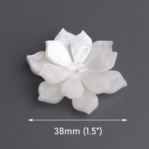 May include: A white, flower-shaped decorative element with multiple petals. The object is 1.5 inches (38mm) in diameter and appears to be made of a translucent material. The flower is set against a gray background.