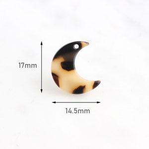 May include: A brown and black crescent moon shaped resin charm with a hole at the top for hanging. The charm measures 17mm tall and 14.5mm wide.