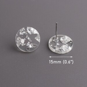 May include: A pair of clear round earrings with silver flakes embedded inside. The earrings are 0.6 inches in diameter.
