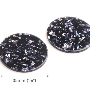 May include: Two black, oval-shaped resin cabochons with a speckled, glittery appearance. Each cabochon measures 1.4 inches (35mm) in diameter. The glitter is a mix of silver and iridescent colors.
