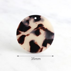 May include: A round, tortoiseshell-patterned pendant with a hole at the top for stringing. The pendant is 35mm in diameter, featuring a mix of cream, dark brown, and black colors. Ideal for jewelry making or crafting.