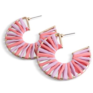 Puede incluir: Un par de pendientes de aro dorados con tejido tejido rosa y morado. El tejido está tejido en un patrón radial, creando un efecto de sol.
