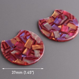 Puede incluir: Dos colgantes en forma de media luna con un patrón de mosaico rojo y dorado. Cada colgante mide 3,7 cm de ancho. El diseño de mosaico presenta una mezcla de tonos rojos, dorados y morados, creando un efecto brillante. Los colgantes tienen un acabado liso y brillante.