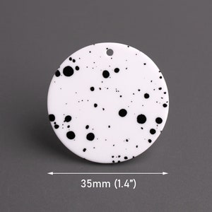 May include: White round acrylic blank with black splatter paint design. The blank measures 35mm in diameter.